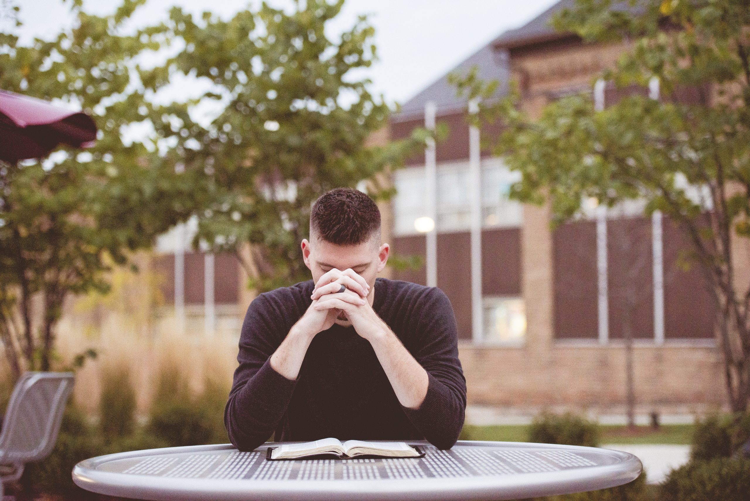 shallow-focus-shot-male-praying-with-open-bible